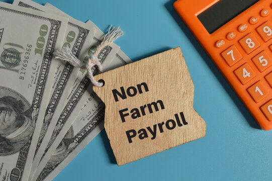 Top view of calculator, money banknotes and wooden board written with NON FARM PAYROLL.