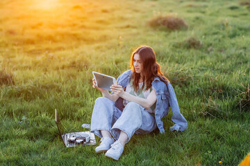 Laughing casual student working with a laptop sitting on green grass in park, Sunset light. Lifestyle concept