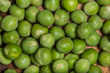 Top view Fresh raw green peas (Pisum sativum) in a wooden bowl with leaves and flower on a wooden table