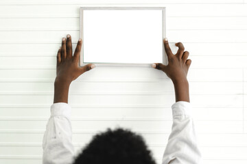 Portrait of black african american cute little boy child hanging and putting picture photo frame blank white mockup on white wall at interior design room