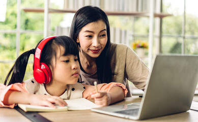 Mother and asian kid little girl learning and looking at laptop computer making homework studying...