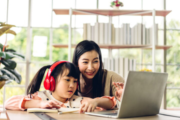 Mother and asian kid little girl learning and looking at laptop computer making homework studying knowledge with online education e-learning system.children video conference with teacher tutor at home