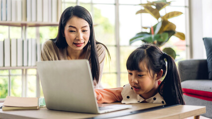 Mother and asian kid little girl learning and looking at laptop computer making homework studying knowledge with online education e-learning system.children video conference with teacher tutor at home