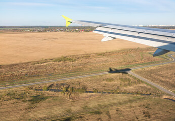 View of airplane wing, Shadow of the plane on the ground during landing, seen from the plane window.