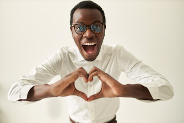 Studio image of happy excited young dark skinned guy wearing spectacles opening mouth widely...