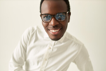 Portrait of cheerful successful young African American manager wearing formal white shirt and eyeglasses posing isolated with broad confident smile, feeling optimistic about future career