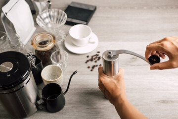 Close up,  Barista use grinder coffee beans with manual stainless steel grinding to make black coffee machine, brewing equipment or coffee drip set Dripper on a wooden table In the kitchen at home - obrazy, fototapety, plakaty