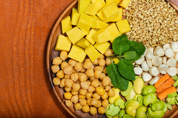 Broad beans, carrots, white corn, mint, chickpea, wheat and squash on wooden bowl. Top view.