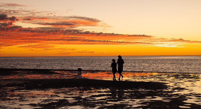 Woman and child walking along beach at sunset in Coral Bay, Western Australia
