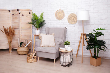 Stylish room with armchair, lamp and plants over brick wall