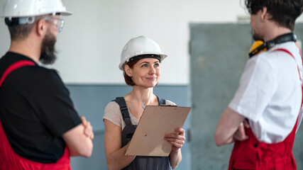 Group of workers with helmet indoors in factory, discussing issues.