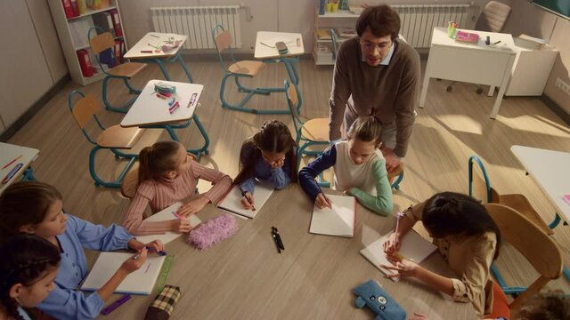 Students sitting at round table in classroom. Teacher explaining task of lesson