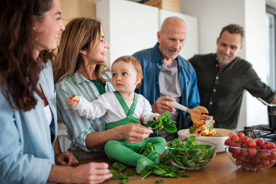 Happy multigeneration family indoors at home preparing vegetable salad.