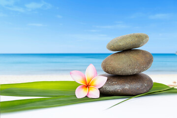Stone stack and Plumeria flower on bamboo leaf over blurred beach background, spa concept, nature background