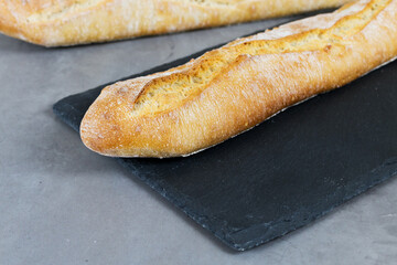 french baguette bread on black cutting board on grey stone background. Diagonal.