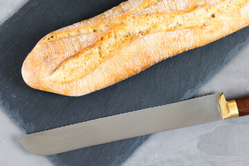 french baguette bread with knife on black cutting board on grey stone background. Diagonal.