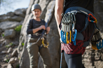 Unrecognizable instructor with harness and carabiners climbing rocks with seniors outdoors in...