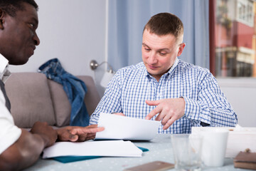 Portrait of interracial men in home interior filling up documents