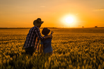 Father and son are standing in their growing wheat field. They are happy because of successful...