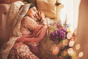 Gorgeous vintage style Indian bride sitting in a luxury hotel room wearing traditional lehenga with ghungat