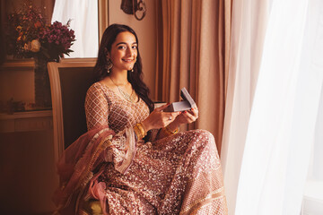 Beautiful Indian woman in a fancy traditional outfit opening the box with present in the luxury five star hotel room, looking at camera
