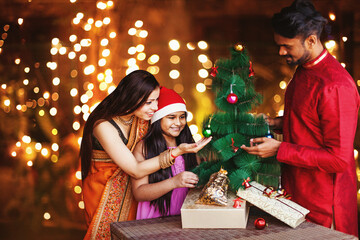 Obraz na płótnie Canvas Beautiful Indian family in ethnic clothes decorating Christmas tree for the New Year celebration at night