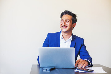 Handsome young professional Indian man in formal suit using laptop in the office over white background
