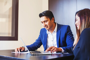 Handsome young Indian professional working on a laptop, training his colleague 