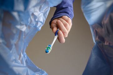 Hand tosses an old plastic toothbrush into the garbage can. An adult male holds a toothbrushing...