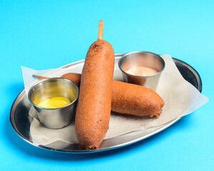 Organic CornDogs on a stick with mustard served on a metal tray over blue background.