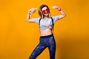 Indoor portrait of laughing girl playing with muscles on yellow background. Shapely young woman in...