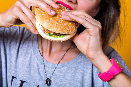 Stylish closeup image of young woman with pink lipstick eating hamburger isolated on yellow background. American style, following tasty fastfood, stylish model with cheeseburger