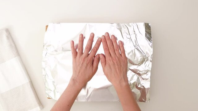 Woman hands cover pan with aluminum foil, close up video, flat lay. Herb roasted turkey leg step by step recipe.