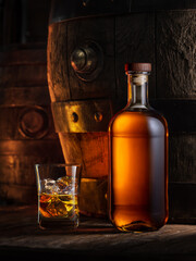 Bottle of whisky and glass of whisky. Old wooden cask at the background.