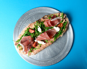 Sandwich with prosciutto, cheese and fresh arugula served on a metal tray over blue background.