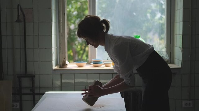 Female potter wearing white shirt, business suit working with clay in workshop