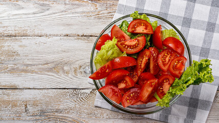 Food banner. Sliced juicy ripe summer tomatoes and crisp lettuce leaves in a glass bowl on a light rustic background. Olive oil and spices salad dressing. Top view. Copy space. Organic farmers food
