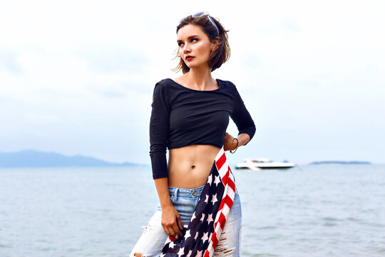 Young beautiful woman posing at sea side, holding american flag
