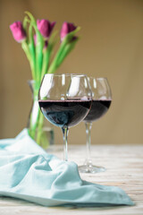 Two glasses of red wine and tulips on a wooden background.