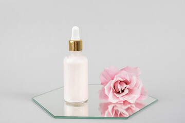 Obraz na płótnie Canvas One glass dropper bottle and pink beautiful flower on mirror, grey background. Natural Organic Spa Cosmetic concept. Front view