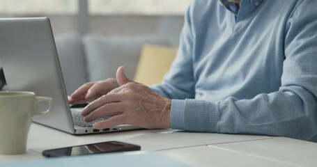 Senior man sitting at desk and using a laptop