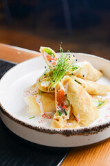 Fresh salmon and cream cheese crepes served in a white plate on a wooden table in restaurant or diner.