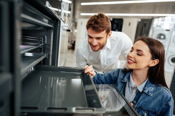 Young couple choosing new electric oven in hypermarket