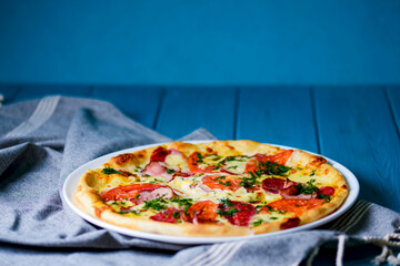 Cooked pizza on aged blue wooden surface background with copy space, side view.