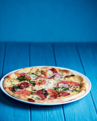 Cooked pizza on aged blue wooden surface background with copy space, side view.
