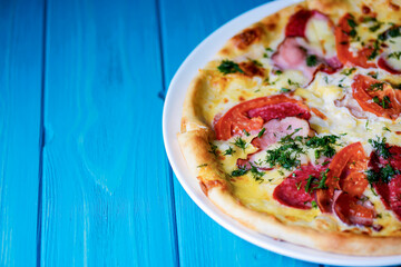 Cooked pizza on aged blue wooden surface background with copy space, side view.
