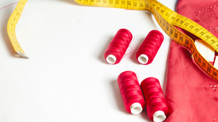 Tailoring accessories. Colorful thread spools with fabric on white table background. Red sewing string. Art, handicraft concept