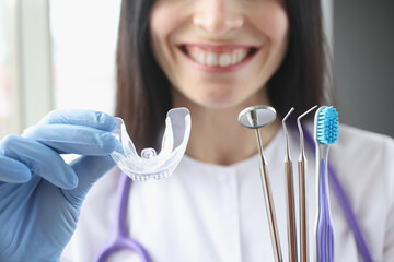 Smiling female doctor holds transparent plastic mouth guard and stomatological instruments in her...