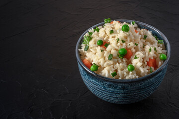 Rice with green peas, carrots, and scallions, on a black background with copy space