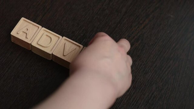 A female hand builds word adverb with wooden cubes. Concept